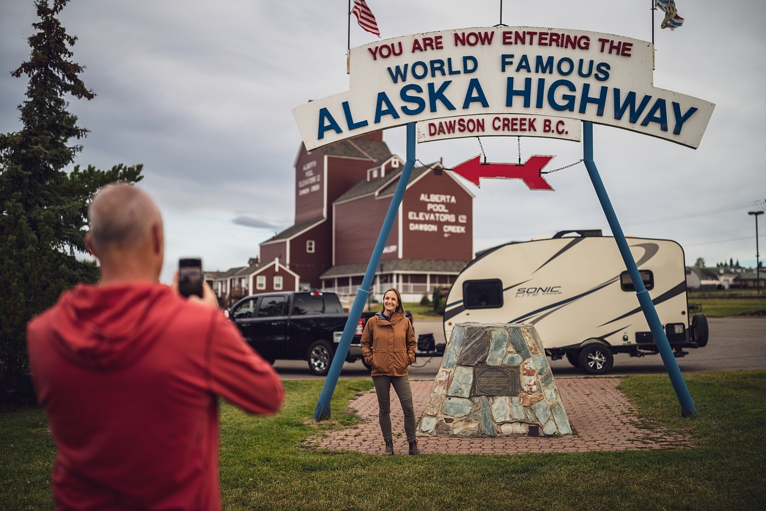 People posing for a photo near a sign that marks Mile Zero of the Alaska Highway in Dawson Creek, BC.