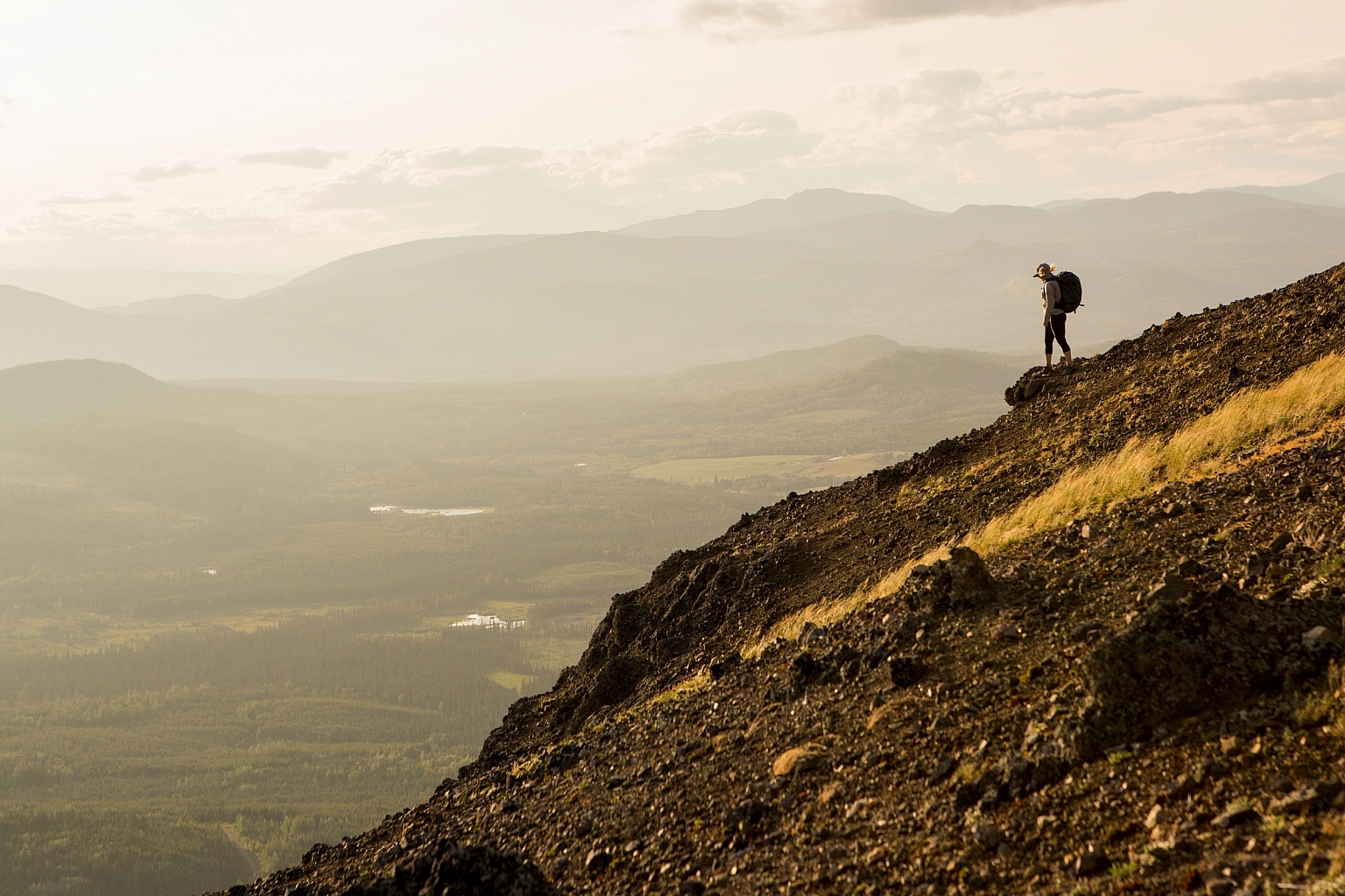 A person is hiking down the China Knows Peak at sunset. The valley is below with mountains in the distance.