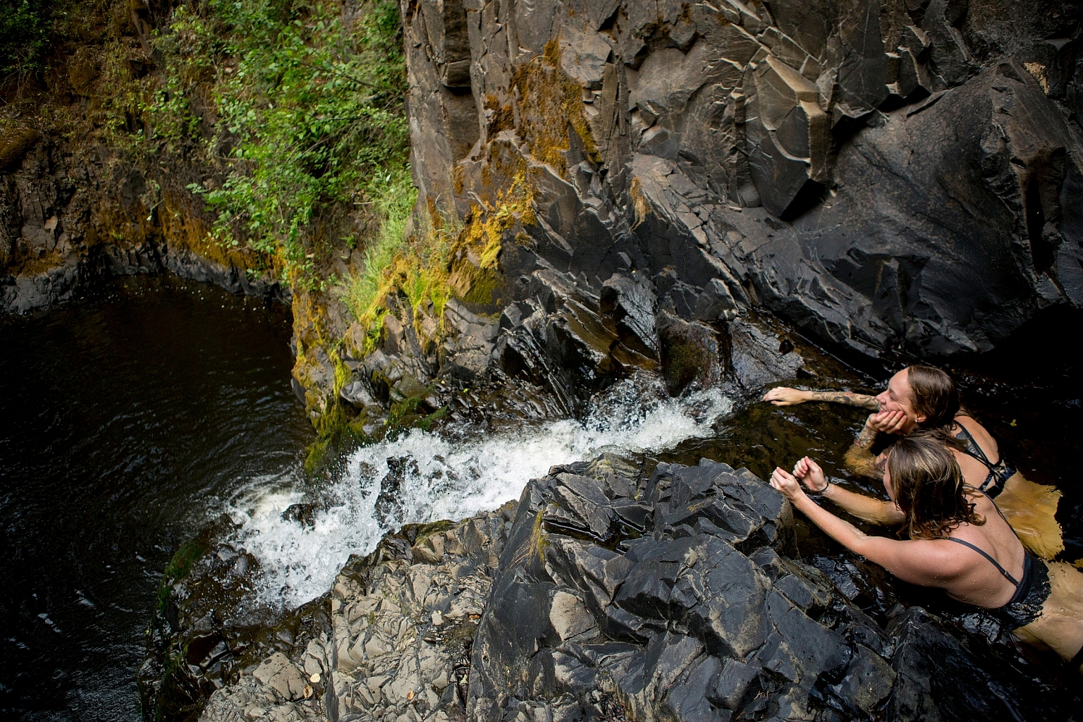 Two women lay down on the rocks, looking down at Aitken Falls.