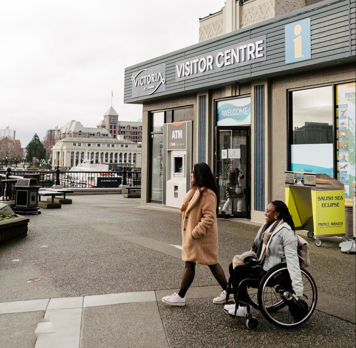 Two people depart the visitor centre in Victoria and move through the parking lot.