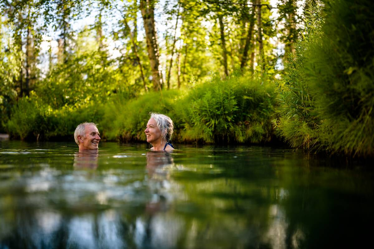 A middle-aged couple soaks in the hot springs, surrounded by forest.